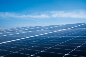 Solar panels mounted on a home rooftop under clear blue sky with leafy trees in the background.